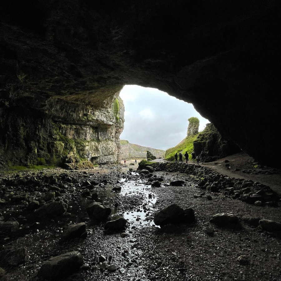 Looking out from inside Smoo Cave, with a stream running over the rocks toward the bright entrance