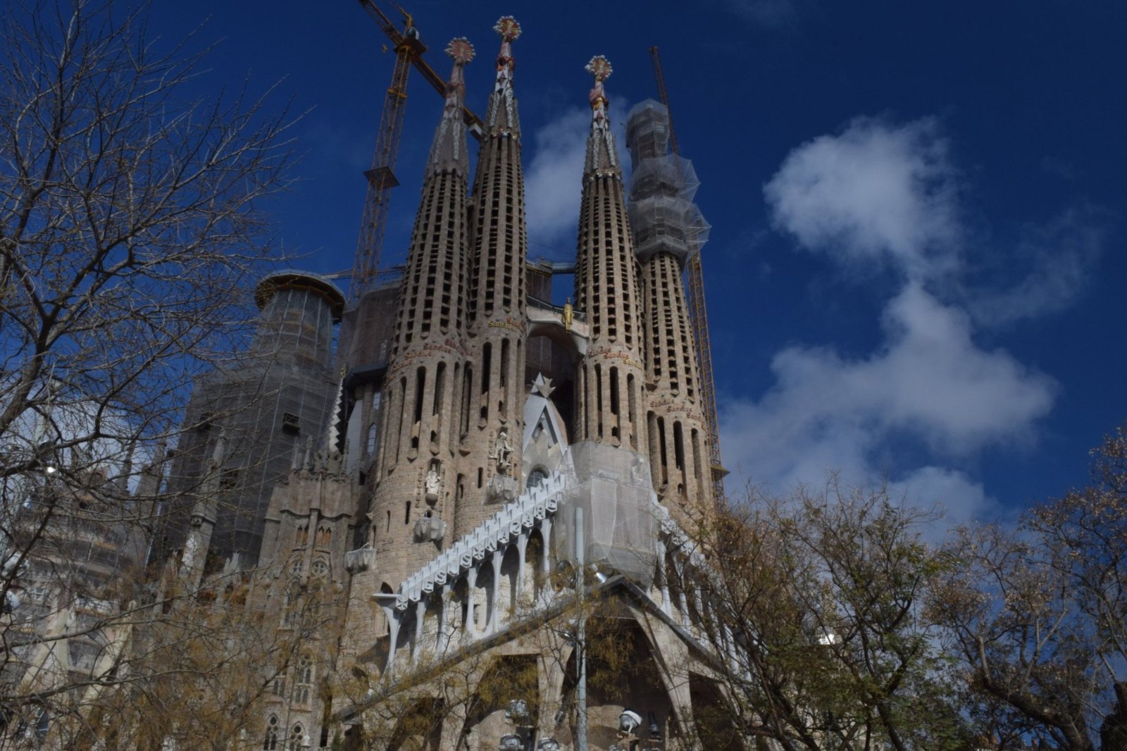 The four spires of the Sagrada Família's Passion façade against a deep blue sky, with a crane behind