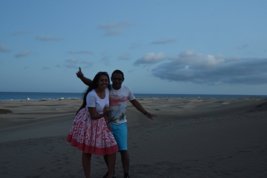 Meenu and Praddy on the dunes at dusk, Praddy waving, with the sea behind