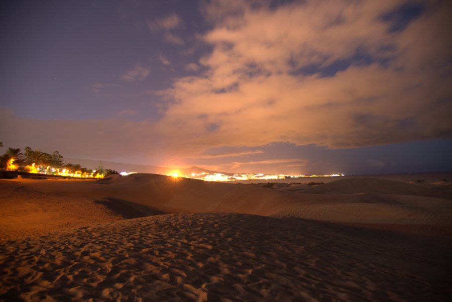 The dunes after dark, with town lights along the horizon and clouds glowing orange above