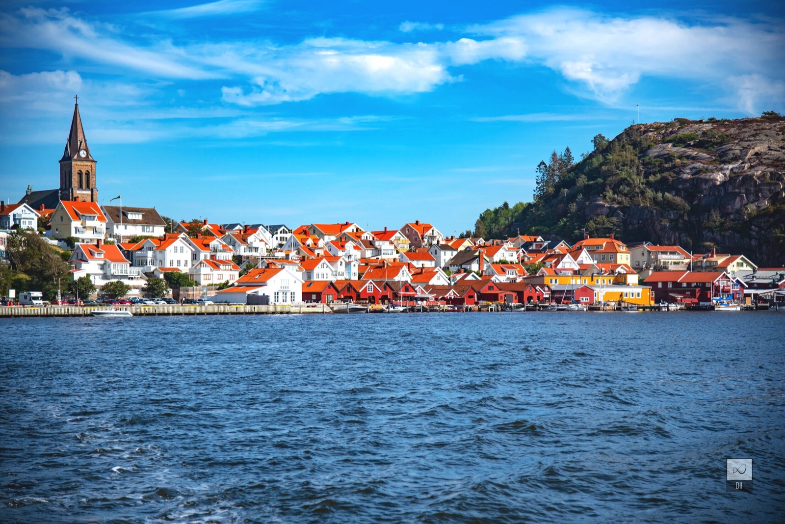 Fjällbacka from the water: white houses with red roofs below a church spire and a granite cliff