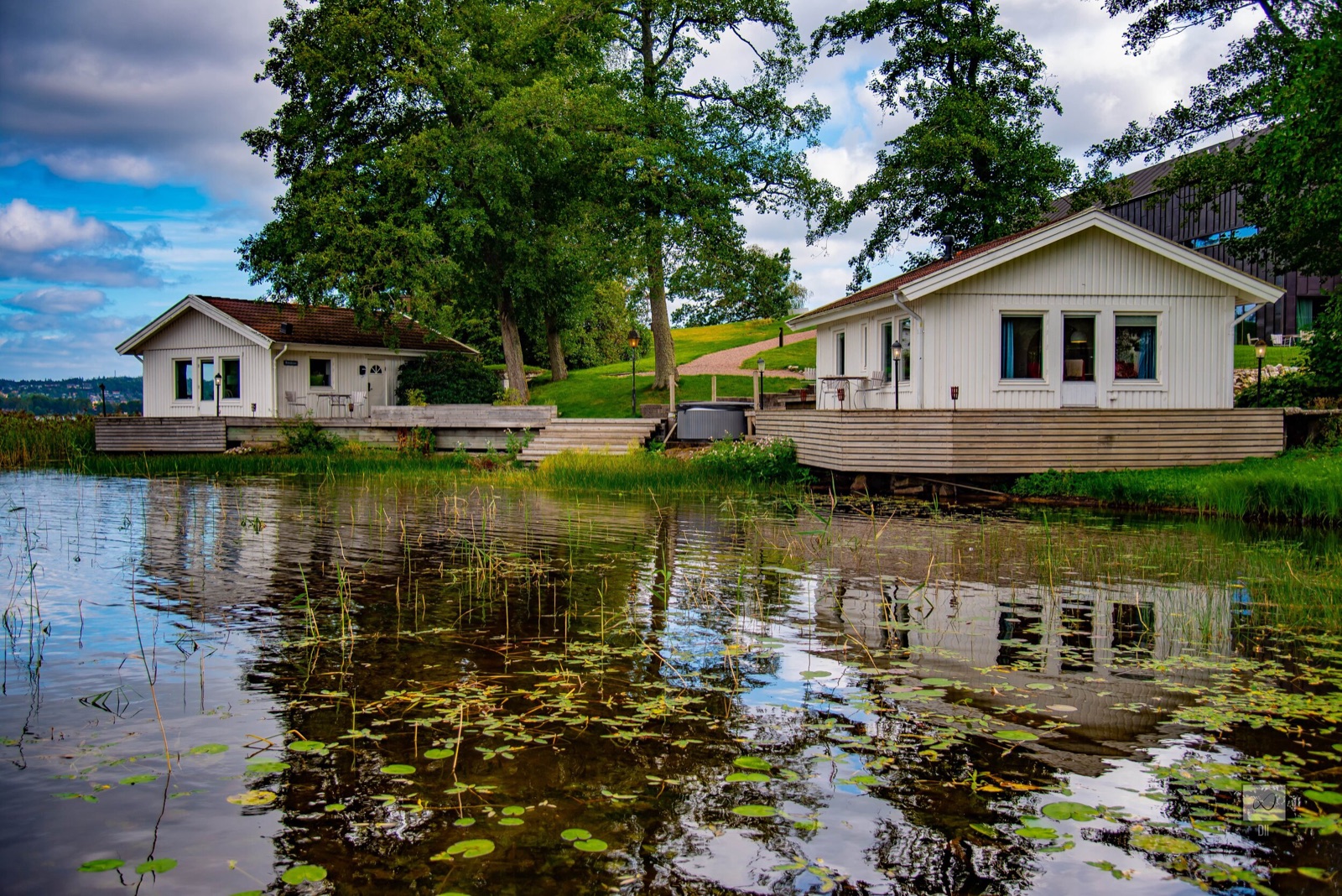 Two white cabins at the edge of a still lake, mirrored in the water among the lily pads