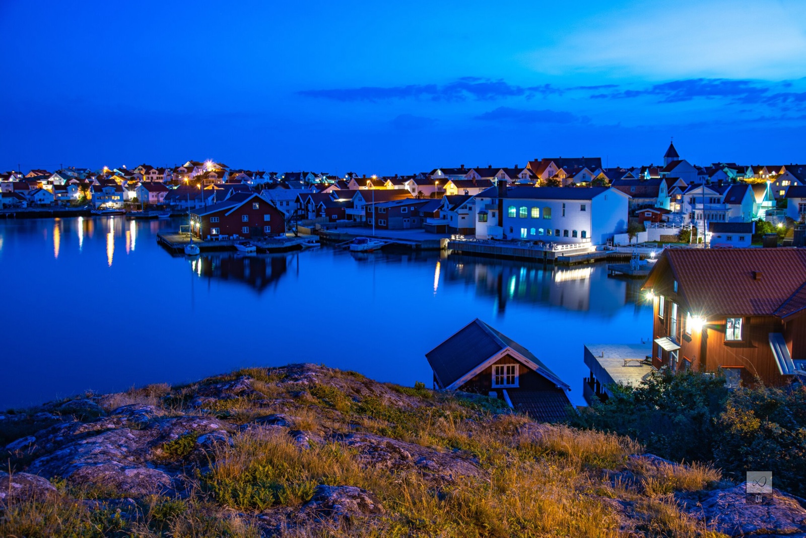 Klädesholmen at blue hour, its lights doubled in the water, with red boathouses below the rocks