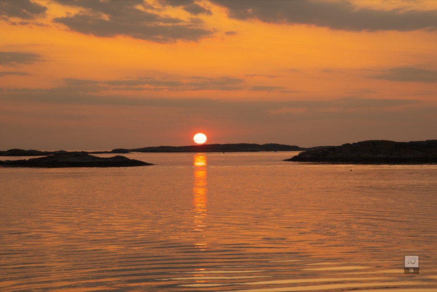 The sun setting into the sea between low islands