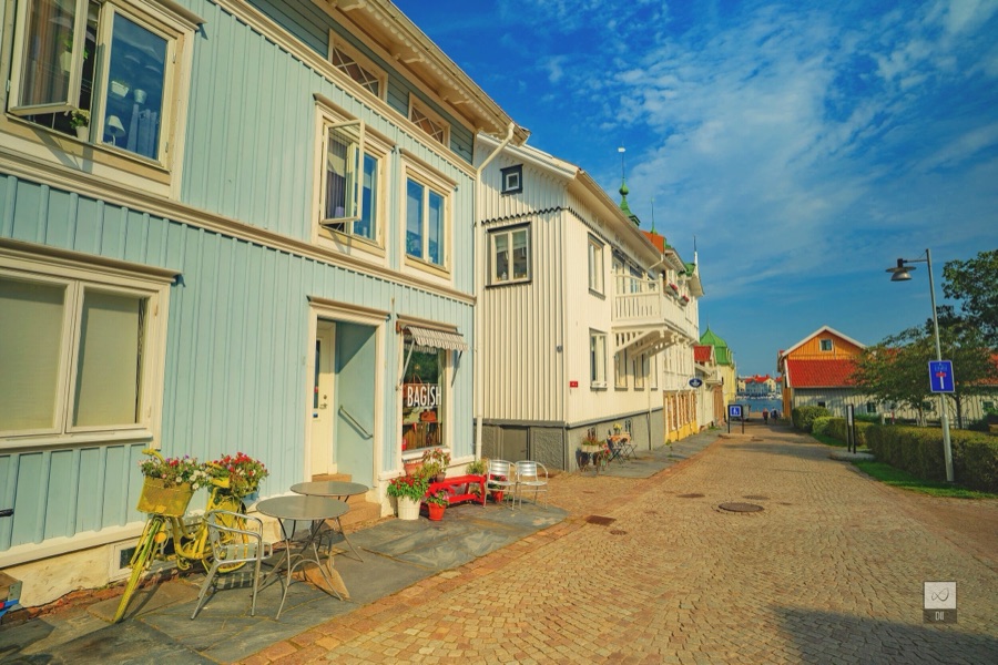 A Marstrand street of pale blue and white wooden houses, with café tables and a yellow bicycle full of flowers