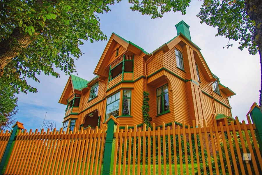 An orange wooden villa with green trim behind an orange picket fence