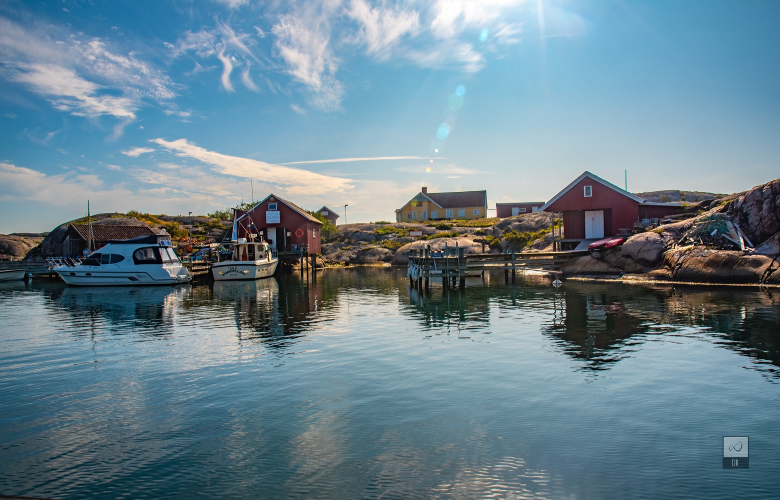 Red boathouses and a moored motorboat mirrored in a sheltered harbour on the Weather Islands