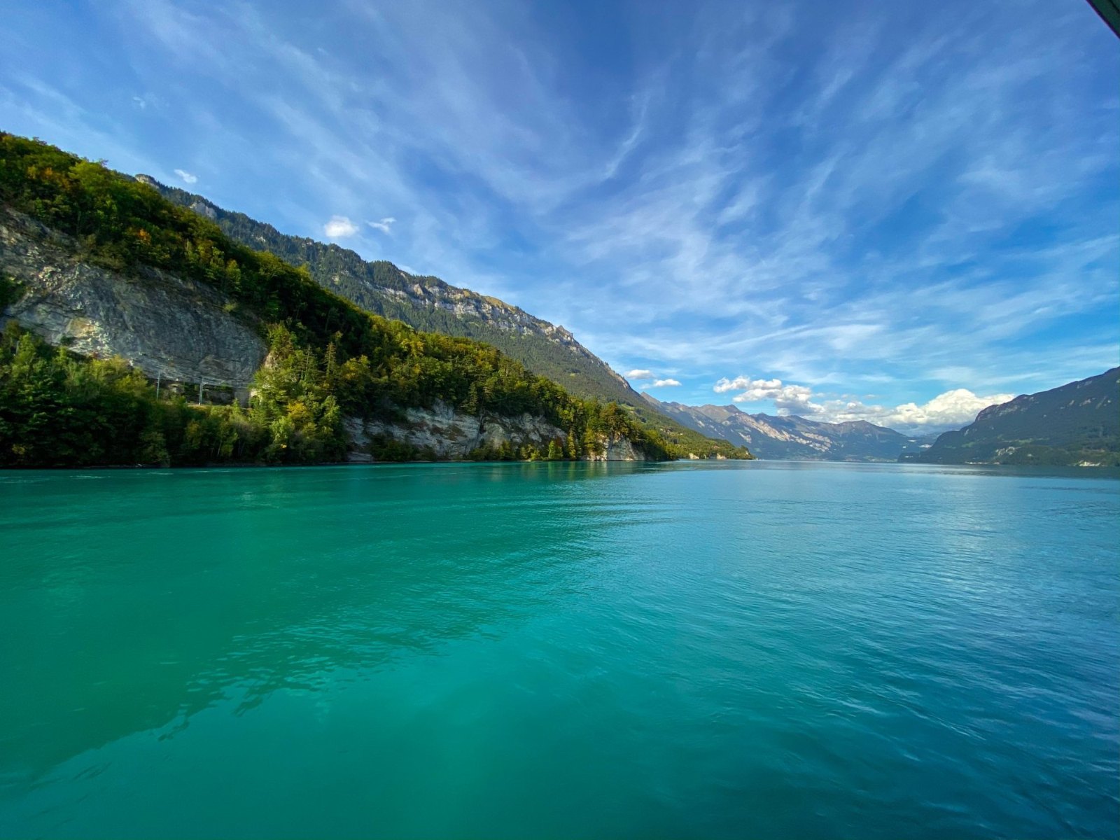 Turquoise Lake Brienz under streaks of cloud, with wooded slopes running down to the water