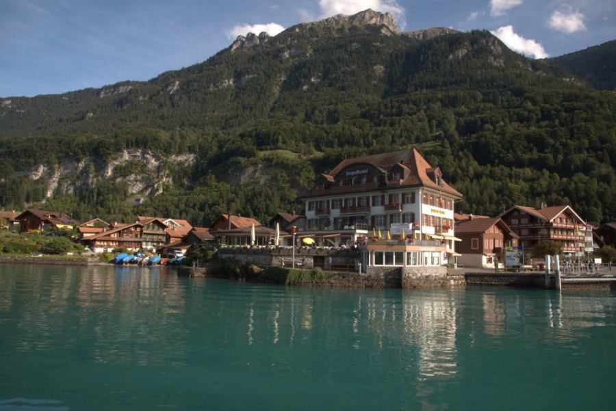 A big chalet with rows of wooden balconies at the water's edge in Iseltwald, seen from the boat