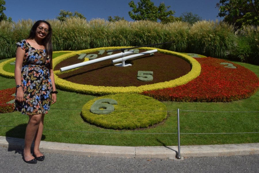 Meenu in a summer dress beside the flower clock, its face planted in red and yellow