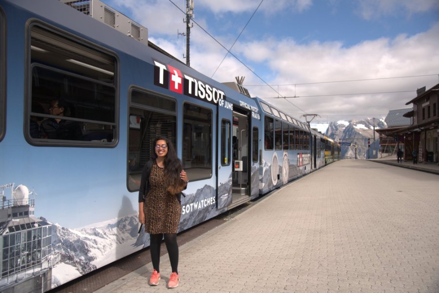 Meenu on the platform beside a Jungfrau Railway train wrapped in a Tissot advert