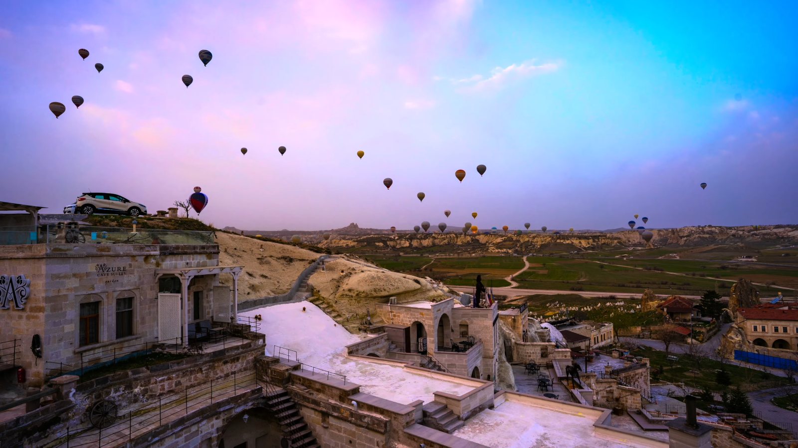Dozens of hot air balloons in a pink dawn sky over the cave houses