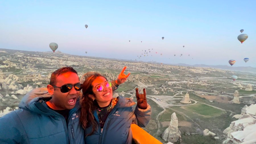 Meenu and Praddy in the balloon basket, with more balloons and the valleys behind