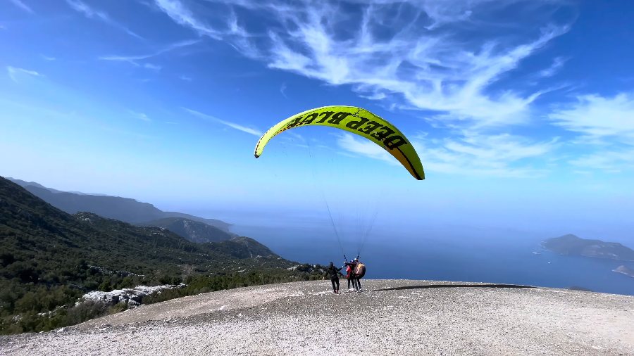 A yellow paraglider lifting off the launch slope above the sea
