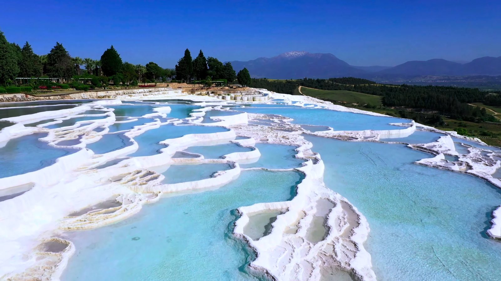 Turquoise pools on Pamukkale's white travertine terraces, with trees and mountains behind