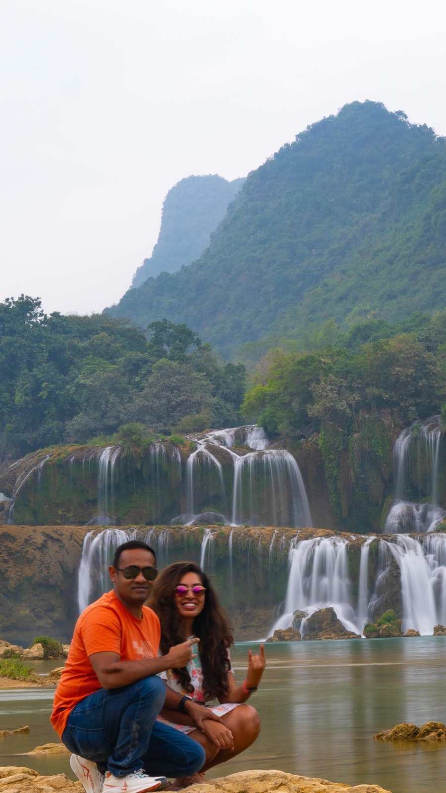 Praddy and Meenu at the foot of Ban Gioc Waterfall, its white falls spilling below a forested mountain