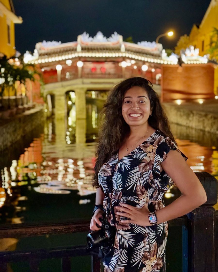 Meenu at night in front of Hội An's Japanese Covered Bridge, lit gold above the water