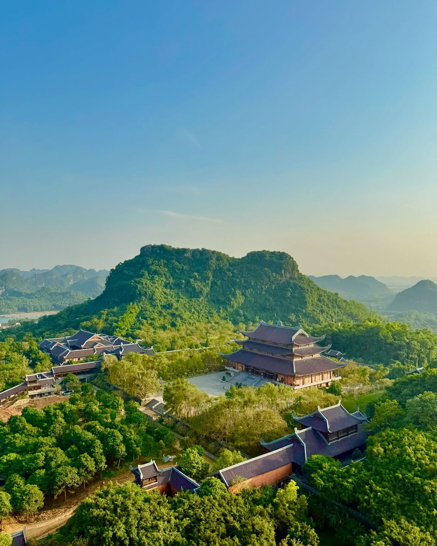 Bái Đính's temple roofs among the trees below a green limestone hill, seen from above