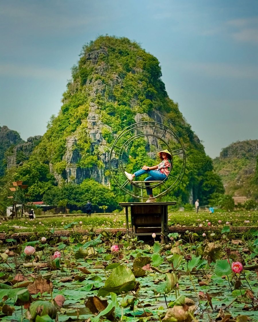 Meenu mid-kick on a post above the water-lily pond at Hang Múa, with a green limestone peak behind