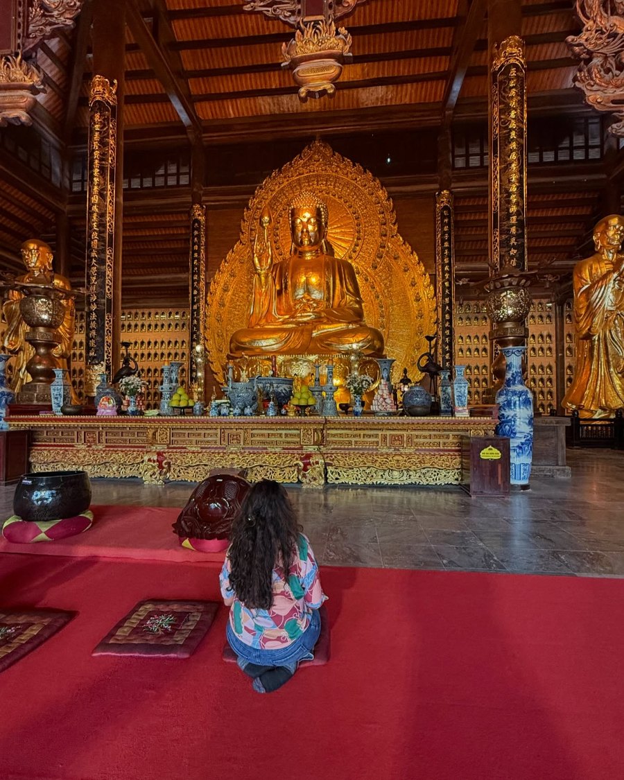 Meenu kneeling before the golden altar of a hall at Bái Đính