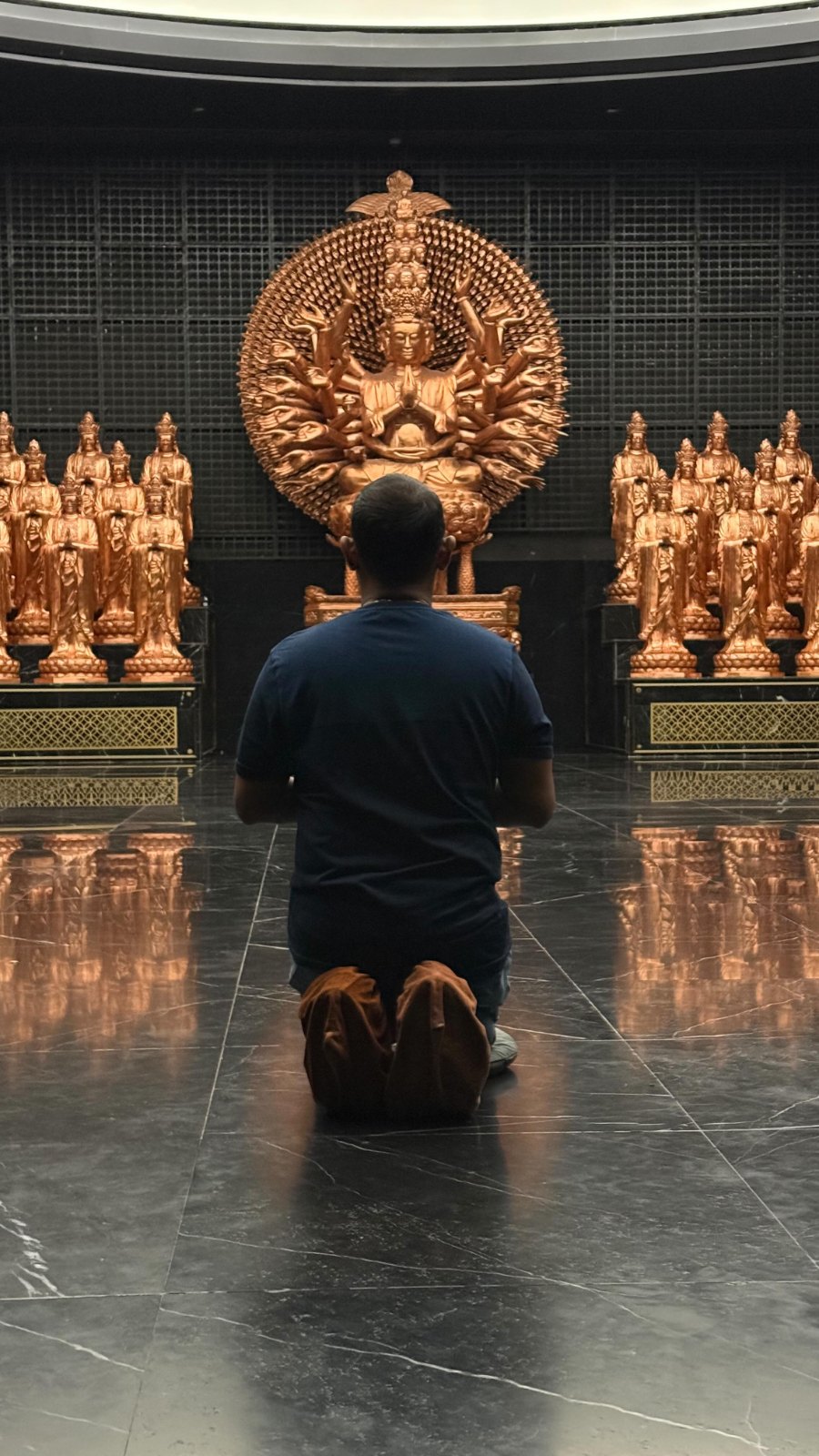 Praddy kneeling before a many-armed golden statue on Núi Bà Đen