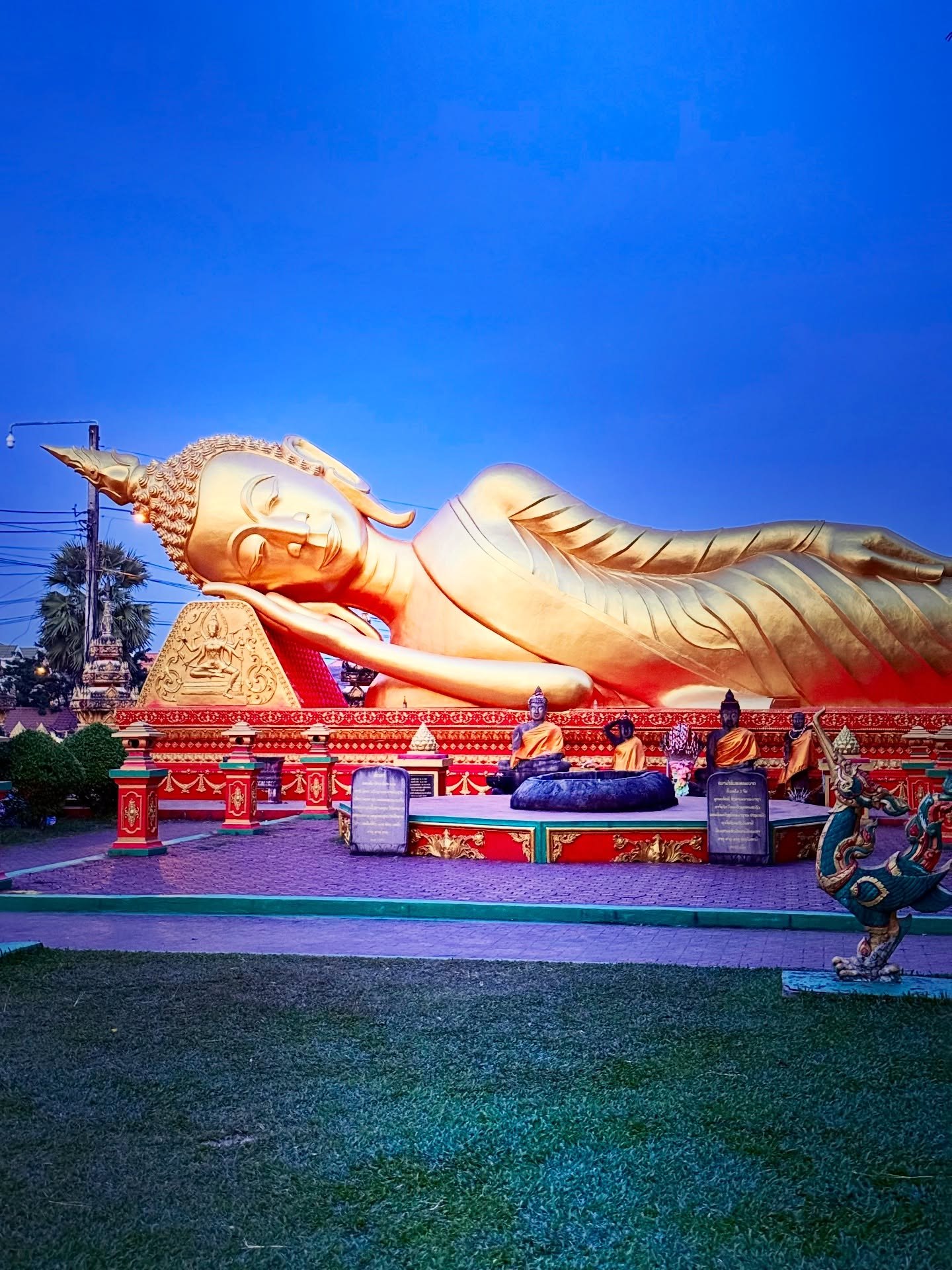 A golden reclining Buddha on a red base under a deep blue sky in Vientiane