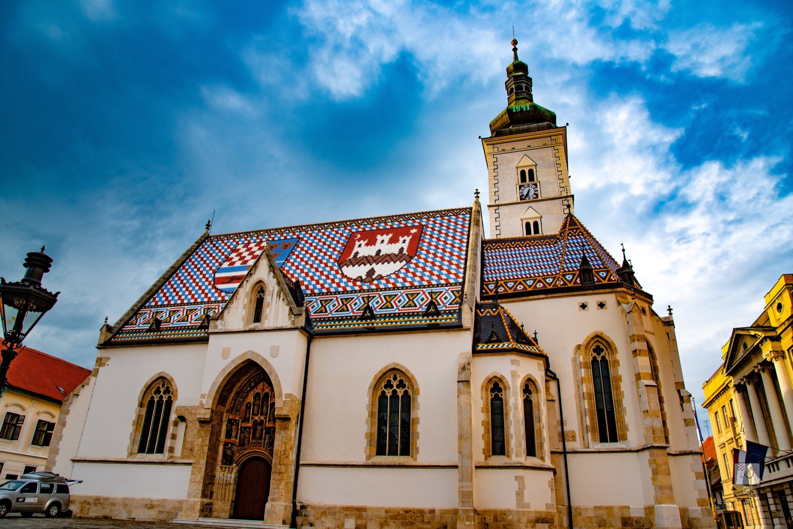 St Mark's Church, its tiled roof patterned with two coats of arms, under a dramatic sky